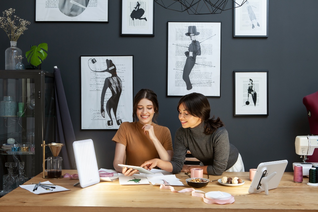 Two female creatives working in front of two Lumie Vitamin L lights receiving bright light therapy